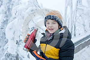 Sweet happy child, drinking hot tea while hiking, playing in deep snow in forest