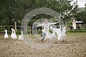 Sweet happy little girl running after a flock of geese on farm his arms to the side and smiling. Lifestyle portrait