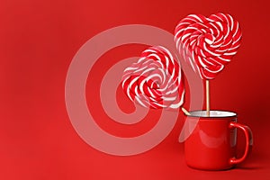 Sweet heart shaped lollipops in cup on red background, space for text. Valentine`s day celebration