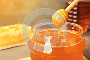 Sweet honey dripping from dipper into glass jar, closeup