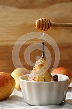 Sweet honey dripping from dipper onto baked pear