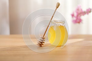 Sweet honey in a glass jar and a honey spoon on a wooden table