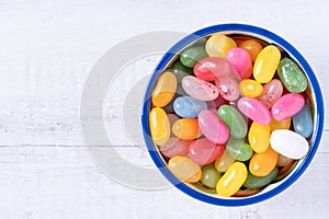 Sweet jelly beans in a ceramic bowl on a white wooden background with copy space. Colorful candy with mixed fruit flavor. Top view