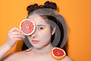 sweet joyful brunette woman girl female with cropped slice of grapefruit near skin face on orange background. tasty