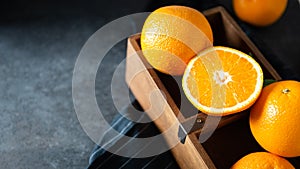 Sweet juicy oranges in a wooden box. Oranges on dark stone background. Pile of oranges close up, copy space. Healthy clean eating