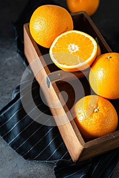Sweet juicy oranges in a wooden box. Oranges on dark stone background. Pile of oranges side view, close up. Healthy clean eating