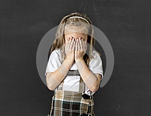 Sweet junior schoolgirl with blonde hair crying sad and shy in front of school class blackboard