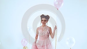 Sweet lady in long pink light luxurious dress with short sleeves walks, holds a helium balloon in her hands, throws up
