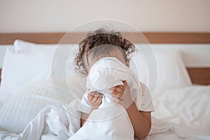 Sweet little baby boy Playing peek-a-boo with a white blanket on the bed