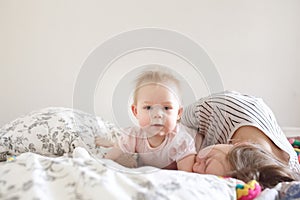 Sweet little baby girl lying on tummy on bed with her mother in morning light