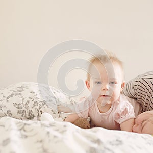 Sweet little baby girl lying on tummy on bed with her mother in morning light