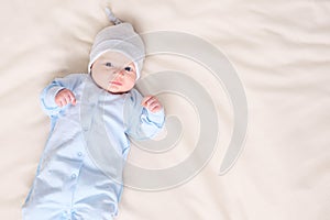 Sweet little baby in warm pajamas and hat lying on comfortable bed at home