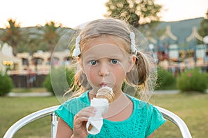 Sweet little blond girl in green t-shirt eating her ice cream in the summer sunshine. Summer vacation, sweet dessert