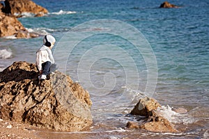 Sweet little boy, sitting on a big rock in the ocean, contemplating