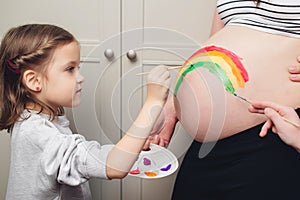 Sweet little daugter painting pregnant belly her mother. Baby birth expecting time and belly painting