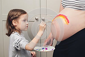 Sweet little daugter painting pregnant belly her mother. Baby birth expecting time and belly painting