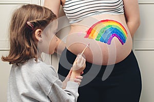 Sweet little daugter painting pregnant belly her mother. Baby birth expecting time and belly painting