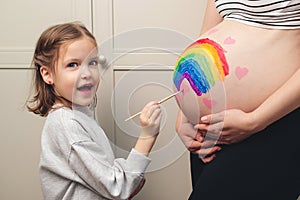 Sweet little daugter painting pregnant belly her mother. Pregnant mom and her child having fun together at home. Family, healthy