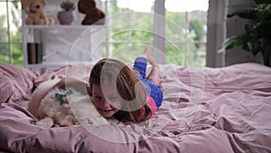 Sweet little girl cuddling sleepy puppy in bed