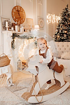 A sweet little girl rides a wooden rocking horse.