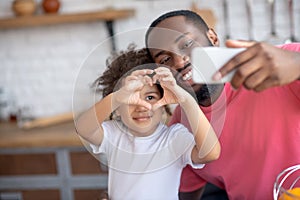 Sweet little girl showing heart sign while her father making selfie