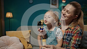 A sweet little girl sits on her mom's lap and blows soap bubbles. Mom and cute little daughter spending time