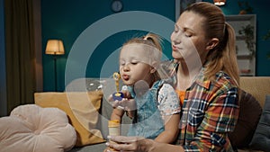 A sweet little girl sits on her mom's lap and blows soap bubbles. Mom and cute little daughter spending time