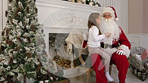 Sweet little girl sitting on Santa lap and describing him what she wants for Christmas