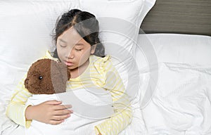 Sweet little girl is sleeping with a teddy bear in her bed at home