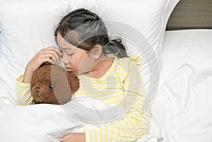 Sweet little girl is sleeping with a teddy bear in her bed at home sweet dream