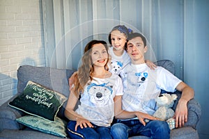 Sweet little girl together with beautiful young mom and dad sitting on sofa in living room at home in evening. Happy family