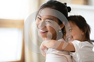 Sweet little preschool asian kid daughter cuddling from back mommy.