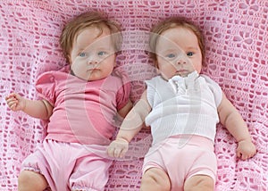 Sweet little twins lying on a pink blanket.
