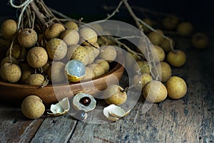 Sweet longan fruit is placed in a wooden round tray and rests on a rustic wooden floor