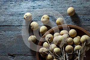 Sweet longan fruit is placed in a wooden round tray and rests on a rustic wooden floor, flat lay