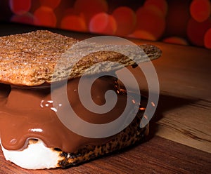 Sweet looking treat of a smore on a wood table with red lights