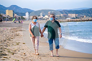 Sweet loving mature couple in face mask during covid19 - senior retired husband and wife on their 70s enjoying beach walk relaxed