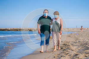 Sweet loving mature couple in face mask during covid19 - senior retired husband and wife on their 70s enjoying beach walk relaxed