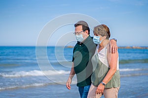 Sweet loving mature couple in face mask during covid19 - senior retired husband and wife on their 70s enjoying beach walk relaxed