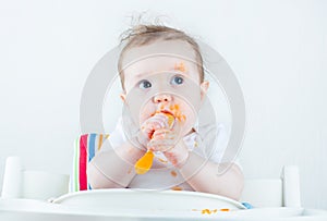 Sweet messy baby eating a carrot in a white high chair