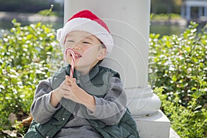 Sweet Mixed Race Boy Wearing Santa Hat Eating Candy Cane