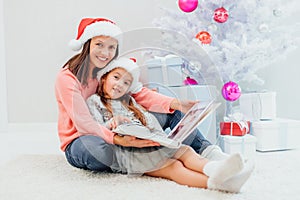 Sweet mother and daughter are looking through the family photo album, recollecting their good old memories on Christmas