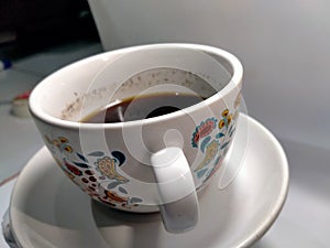 The sweet of a mug black coffee is occurring on the  left behind of the white background surface