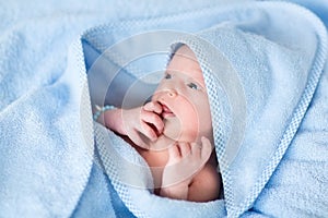 Sweet newborn baby boy in big blue towel after bath