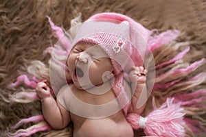 Sweet newborn baby in pink cap yawns and stretches, wakes