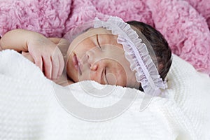 Sweet newborn girl wrapped in a pink and white blanket sleeping peacefully