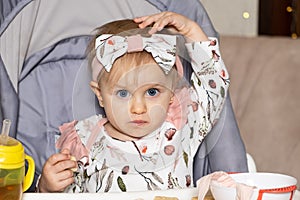 A sweet one-and-a-half-year-old girl sits in a high baby feeding chair and eats cookies.