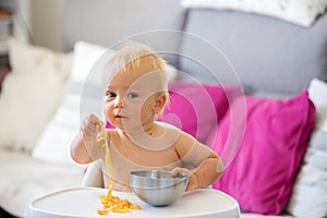 Sweet one years old baby boy, eating pasta at home, kid eats spaghetti