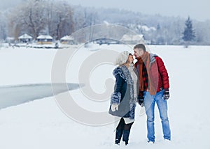 Sweet outdoor portrait of the cheerful loving couple holding hands and almost kissing in the snowy village.
