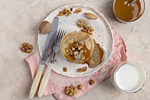 Sweet pancakes with boiled condensed milk and walnuts on plate with fork and knife, milk in glass and caramel in jar near, at